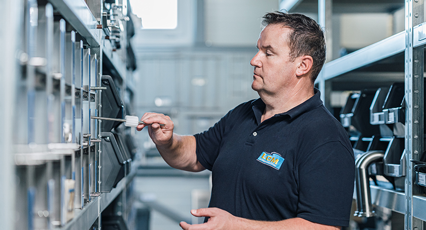 LCM-Mitarbeiter durchsucht Regale im Lager und entnimmt mit einem Werkzeug ein Bauteil.